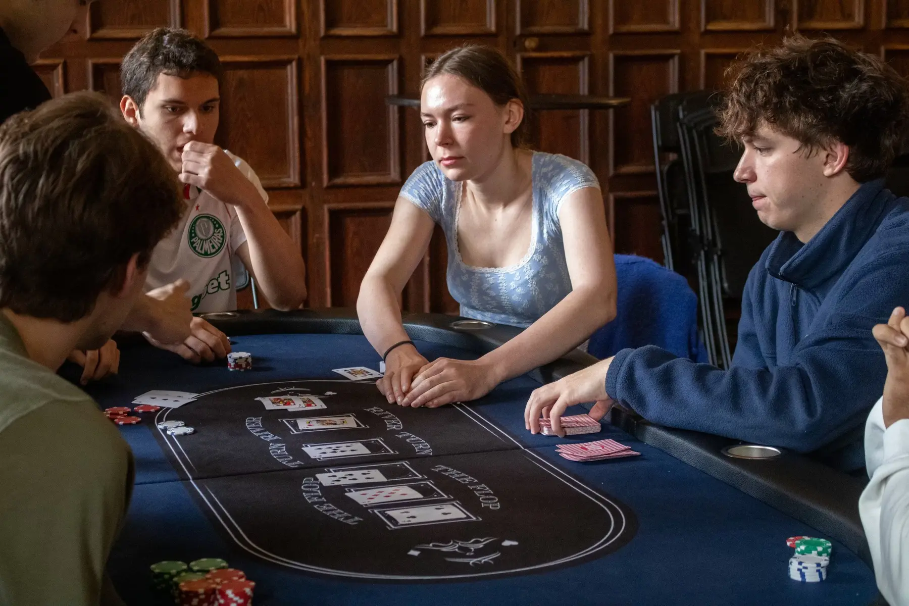 Three club members mid-hand at a poker table in a wood-paneled room